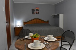 A neatly arranged bedroom with a bed, bedside table, lamp, and a dining table set for breakfast. - Aspid Apartments (Oranjestad)