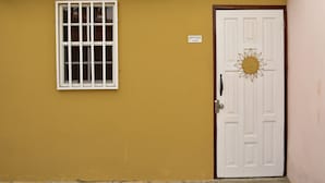 A building with a yellow wall, a white door with a sun decoration, and a window with white frames. - Aspid Apartments (Oranjestad)