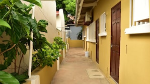 A narrow alleyway with yellow walls, a concrete floor, and a wooden door at the end. - Aspid Apartments (Oranjestad)