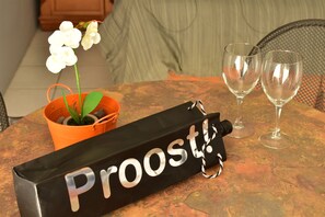 A table with a black box labeled "Proost!", two empty wine glasses, and an orange flower pot with a white orchid. - Aspid Apartments (Oranjestad)