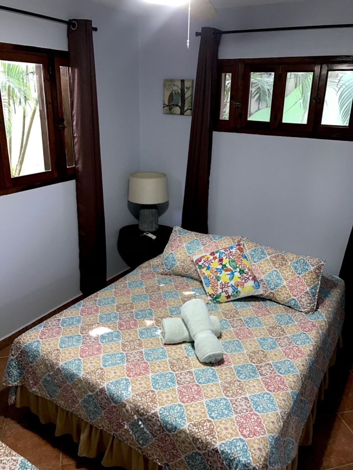 A bedroom with a bed, a nightstand, a lamp, and a window with curtains.