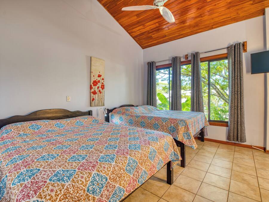 A room with two beds, a ceiling fan, a TV, and a window with curtains.