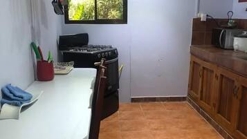 A compact kitchen with a gas stove, a microwave, and a small window.