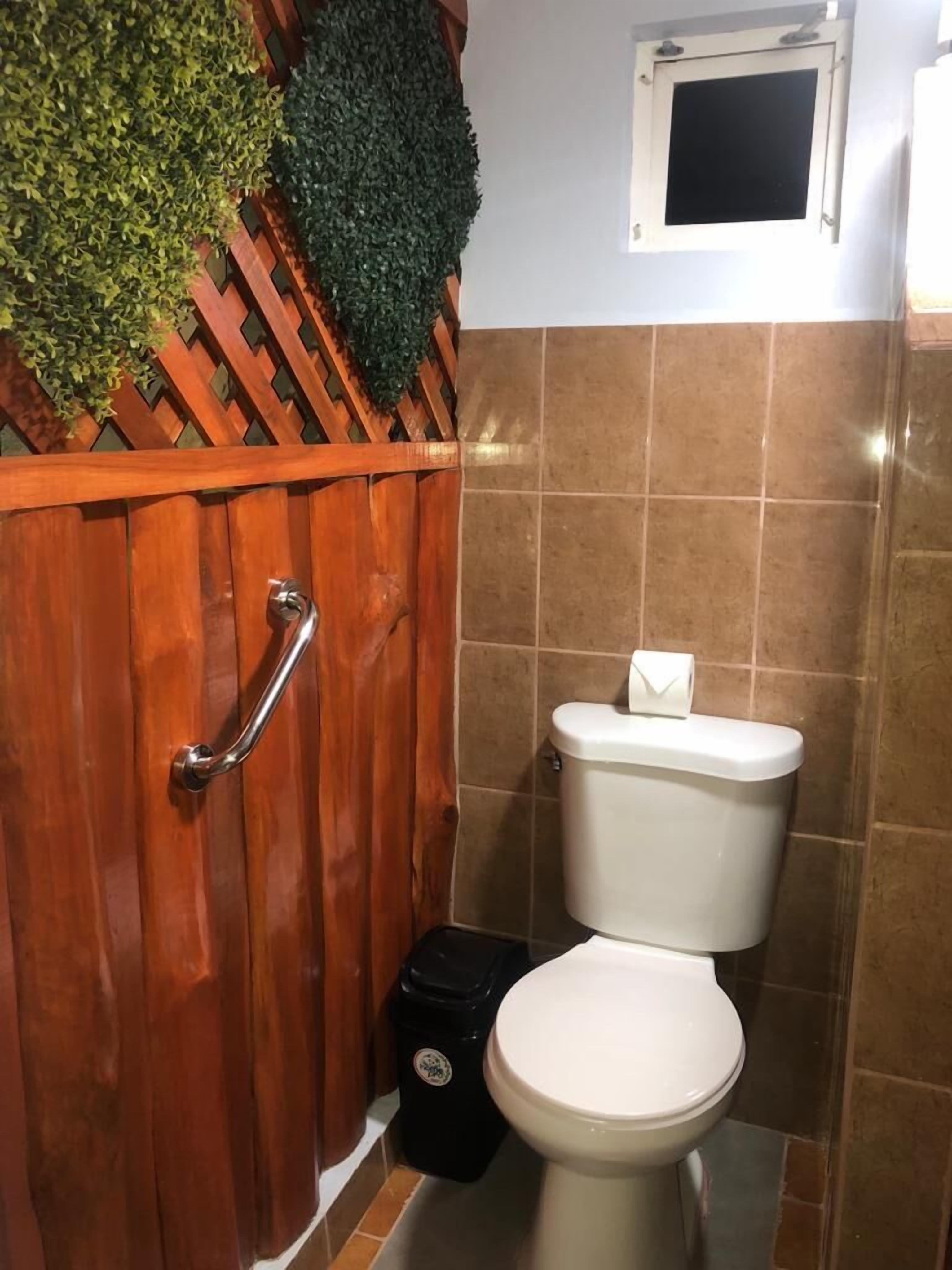 A bathroom with a wooden partition, a toilet, and a trash bin.