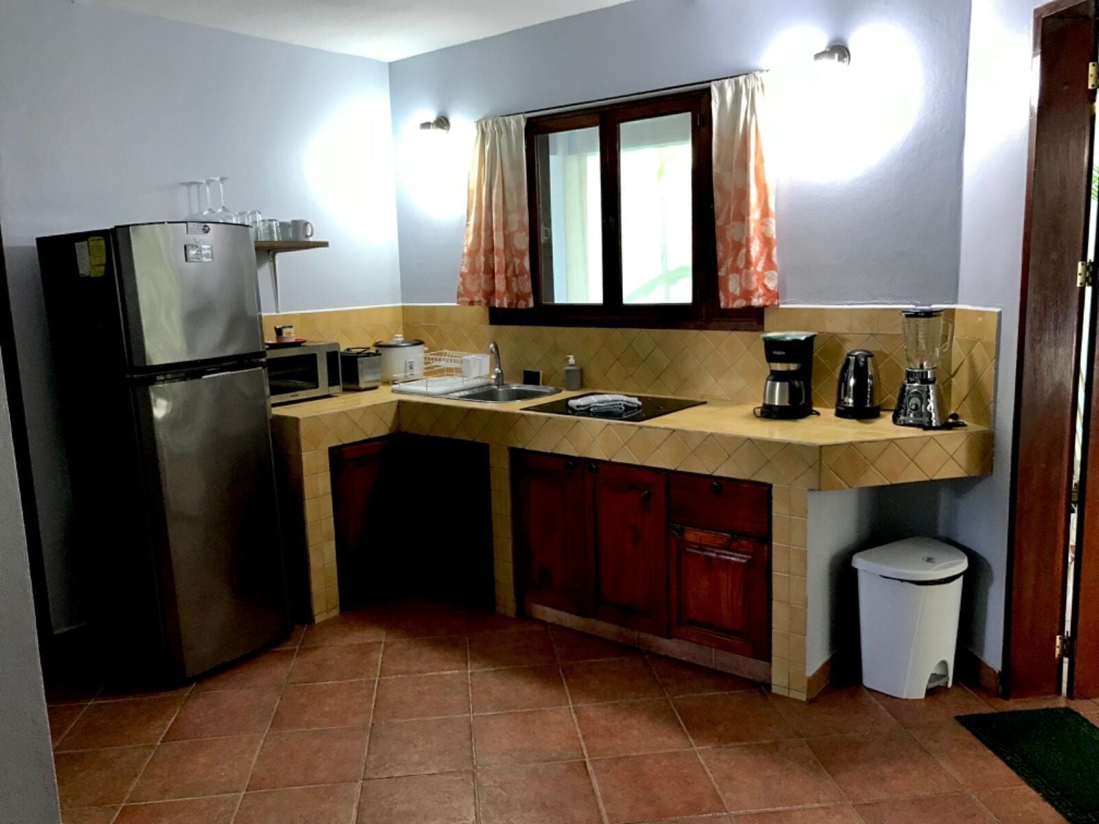 Cocina compacta con refrigerador, microondas, lavaplatos y una pequeña zona de encimera con cafetera y licuadora.