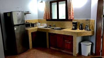 Cocina compacta con refrigerador, microondas, lavaplatos y una pequeña zona de encimera con cafetera y licuadora.