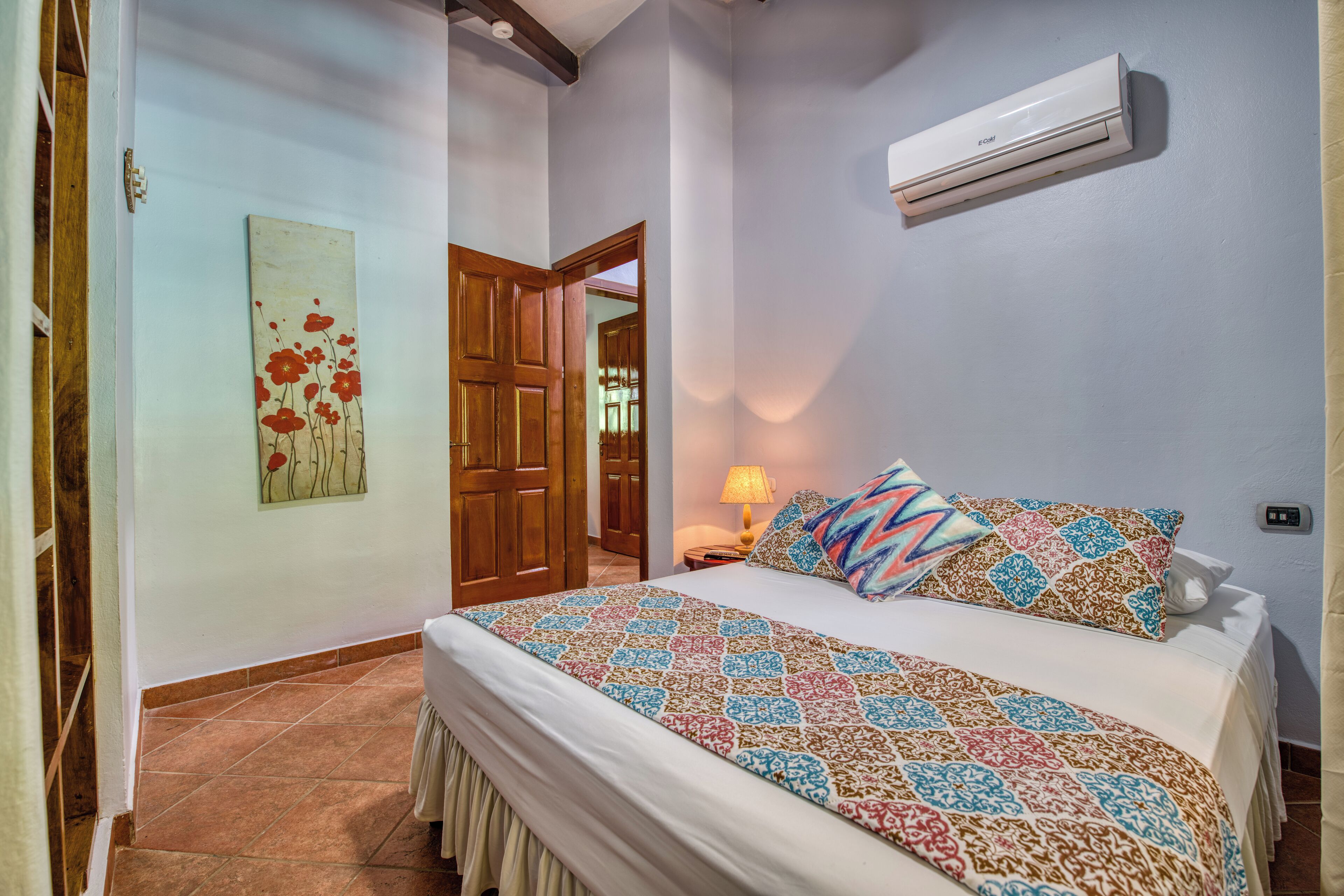 A bedroom with a bed, a wall-mounted air conditioner, a door, and a painting.