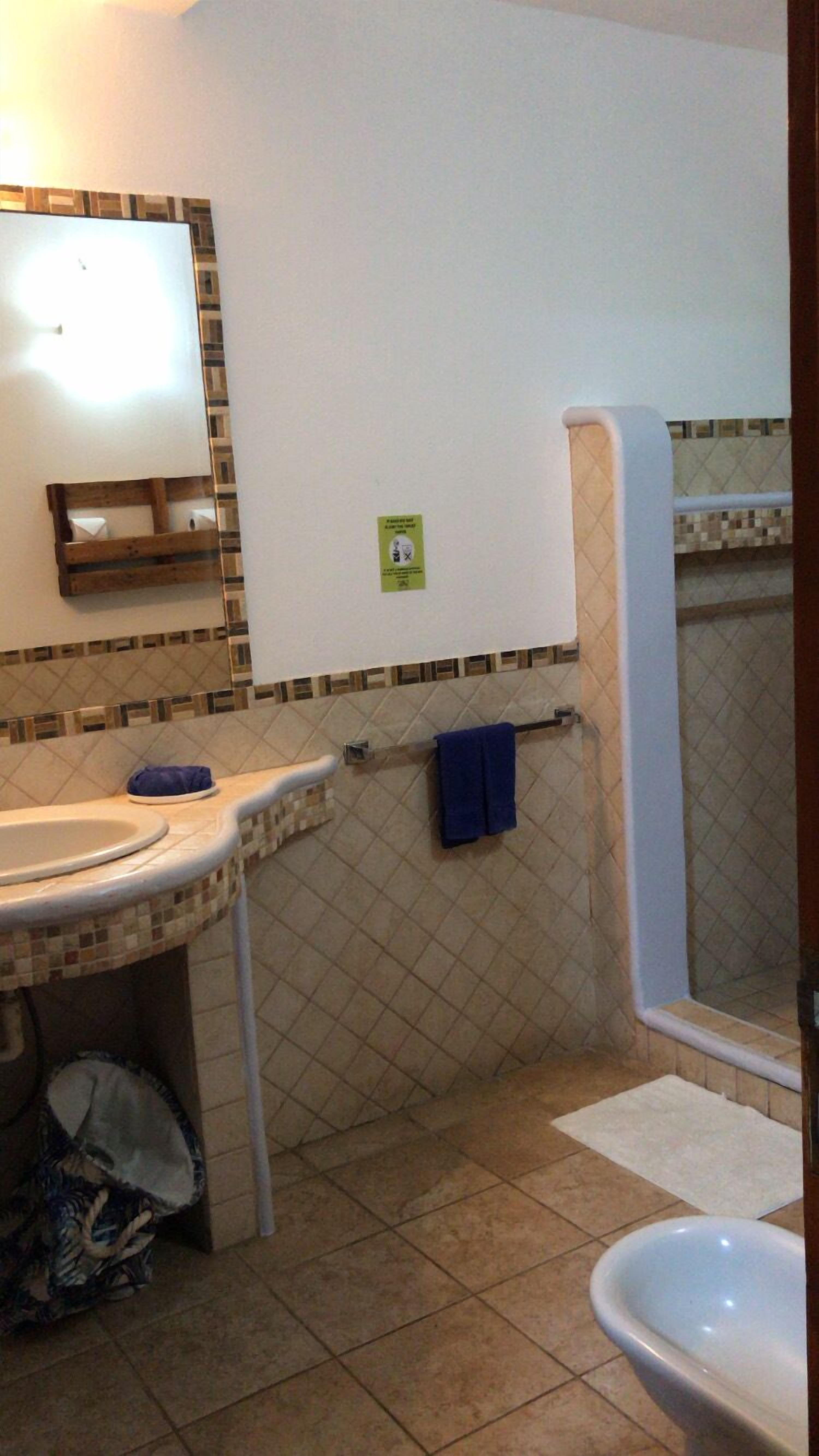 A bathroom with a sink, mirror, and toilet. There is a towel rack with a blue towel. The floor is tiled.