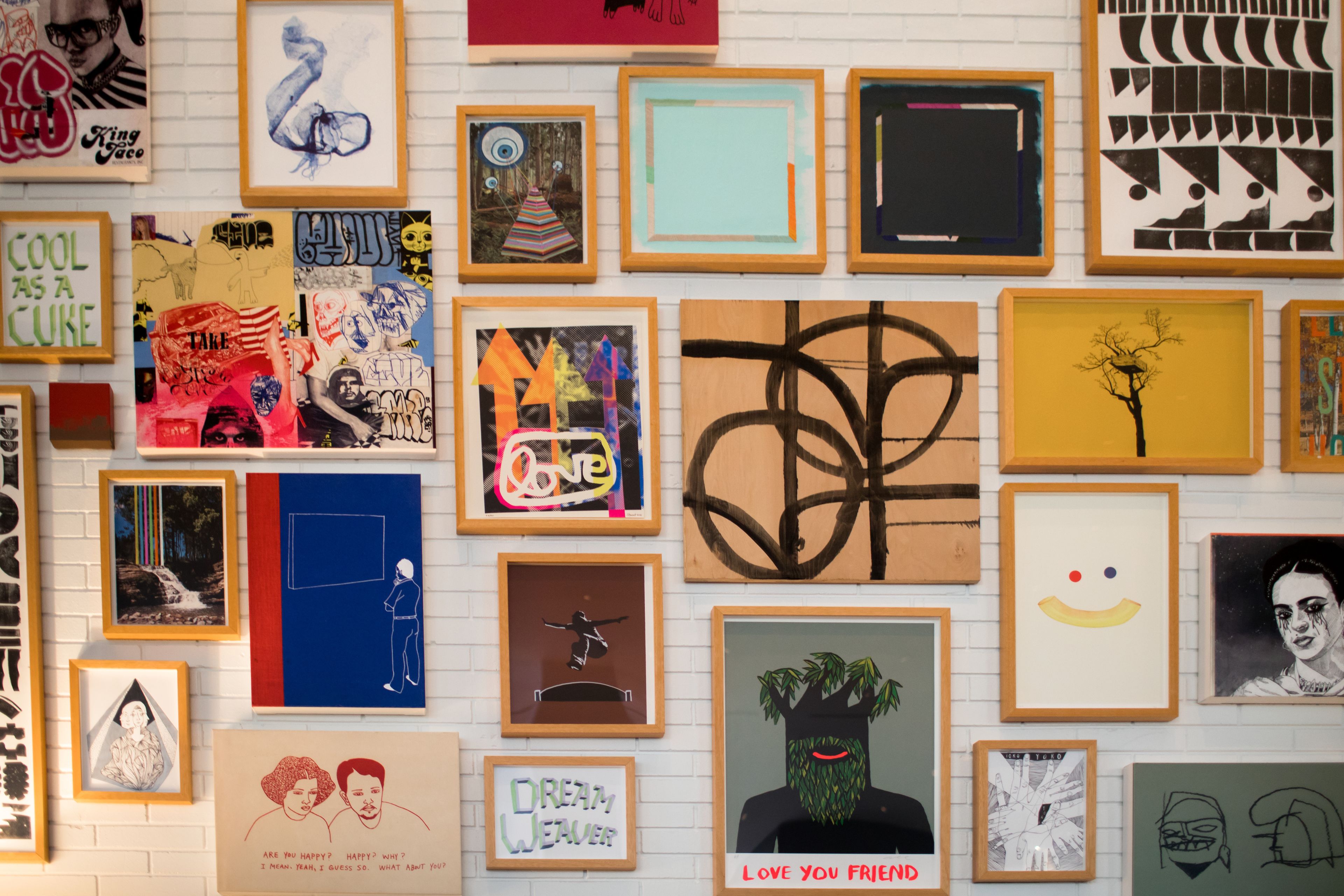 A wall with various framed artworks, including abstract designs, portraits, and text-based pieces.