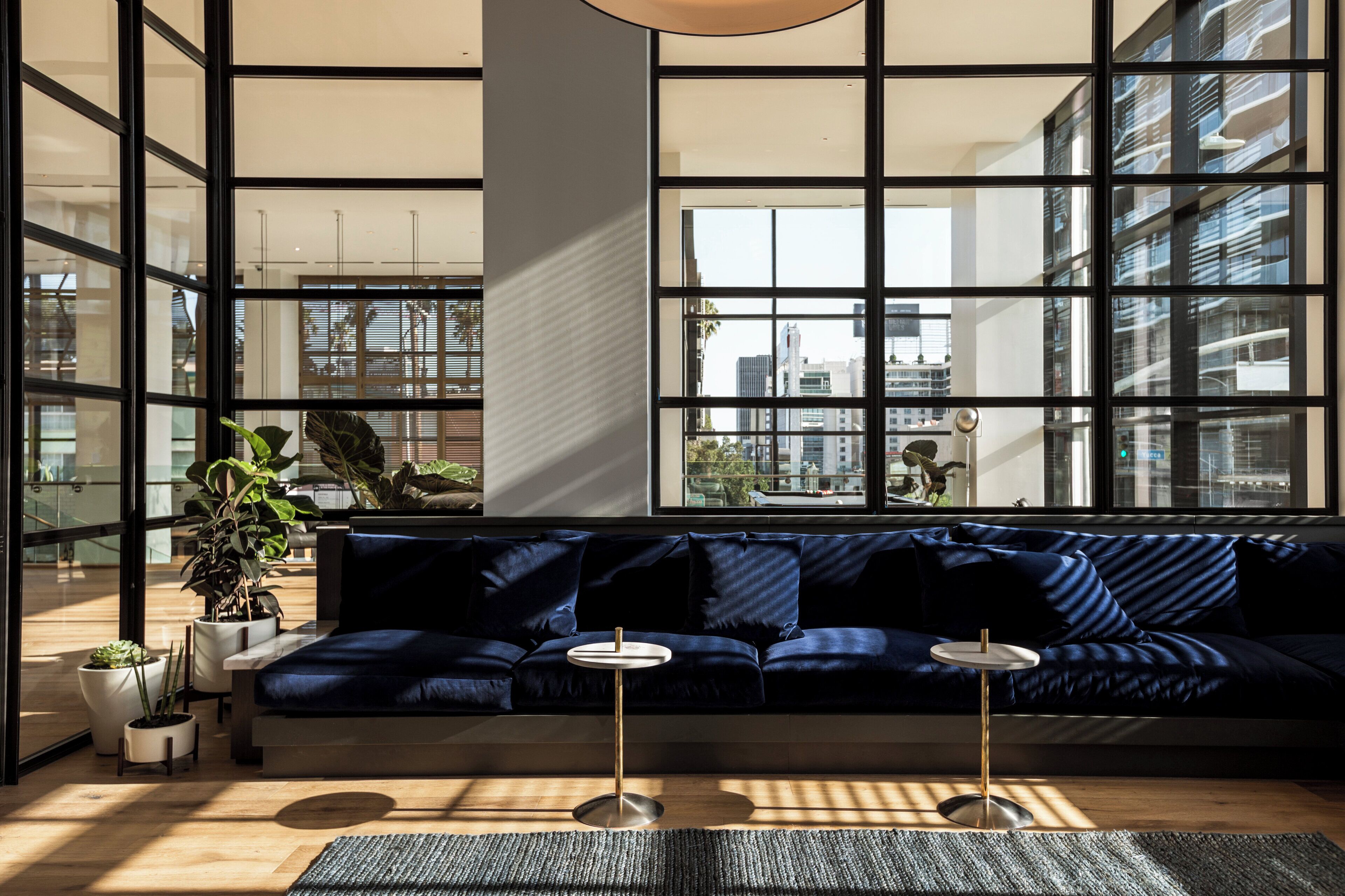 Ein modernes Interieur mit einem dunkelblauen Sofa, zwei kleinen runden Tischen und einem großen Fenster mit Blick auf die Stadtlandschaft.