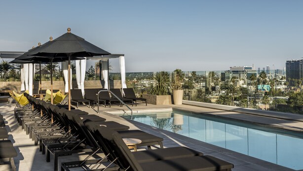 Uma piscina no terraço com espreguiçadeiras e um gazebo, com vista para a cidade.