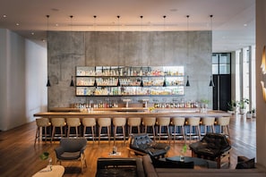 A modern bar area with a high bar, multiple seating options including bar stools and cushioned chairs, and a variety of bottles and glasses on the shelves. - Kimpton Everly Hotel Hollywood by IHG (Los Angeles)