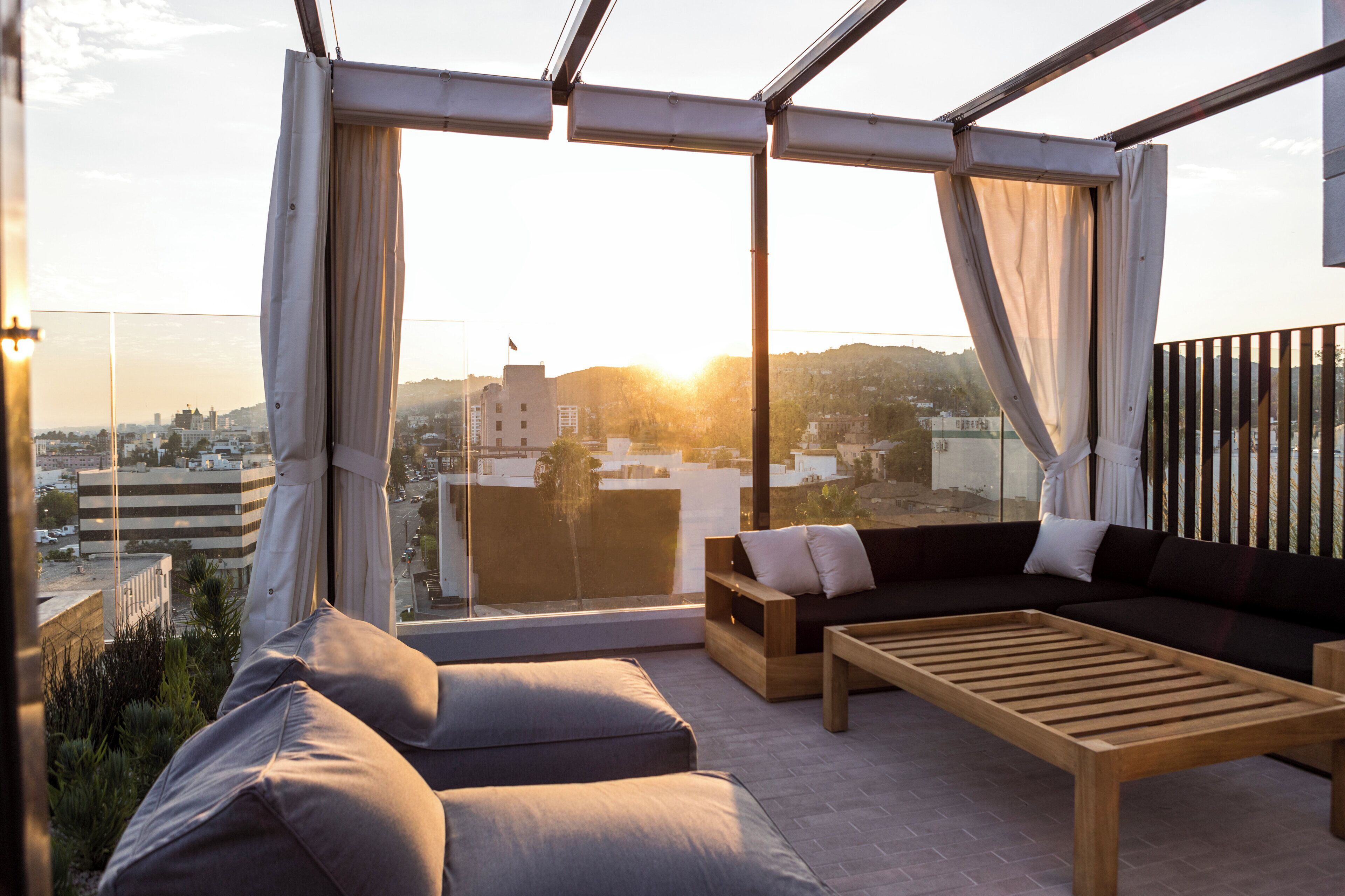 Un espace extérieur moderne aménagé avec un canapé et une table basse, offrant une vue sur le paysage urbain au coucher du soleil.