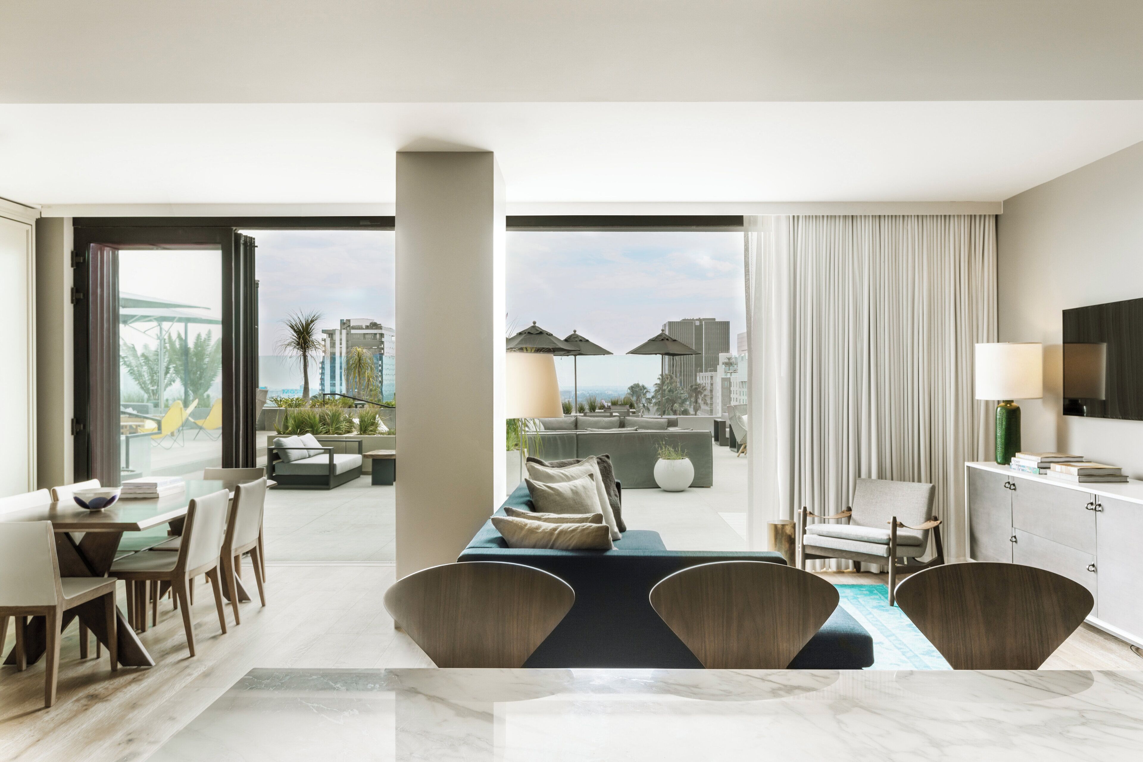 Une chambre d’hôtel moderne dotée d’un coin repas, d’un canapé, d’une télévision et offrant une vue sur le paysage urbain.