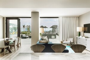 A modern hotel room with a dining area, a sofa, a TV, and a view of the cityscape.
