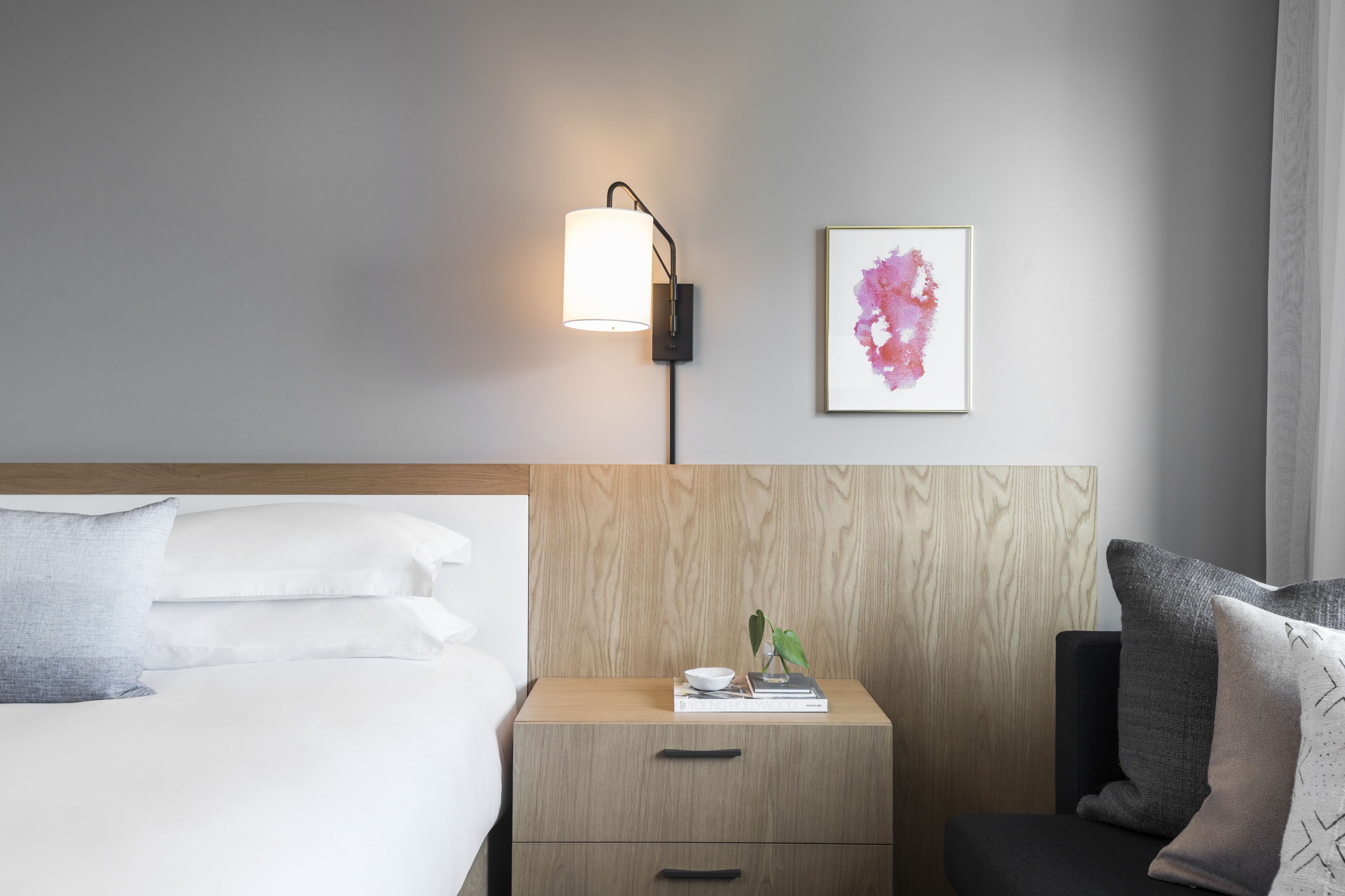 A hotel room with a bed, bedside table, lamp, and a framed artwork on the wall.