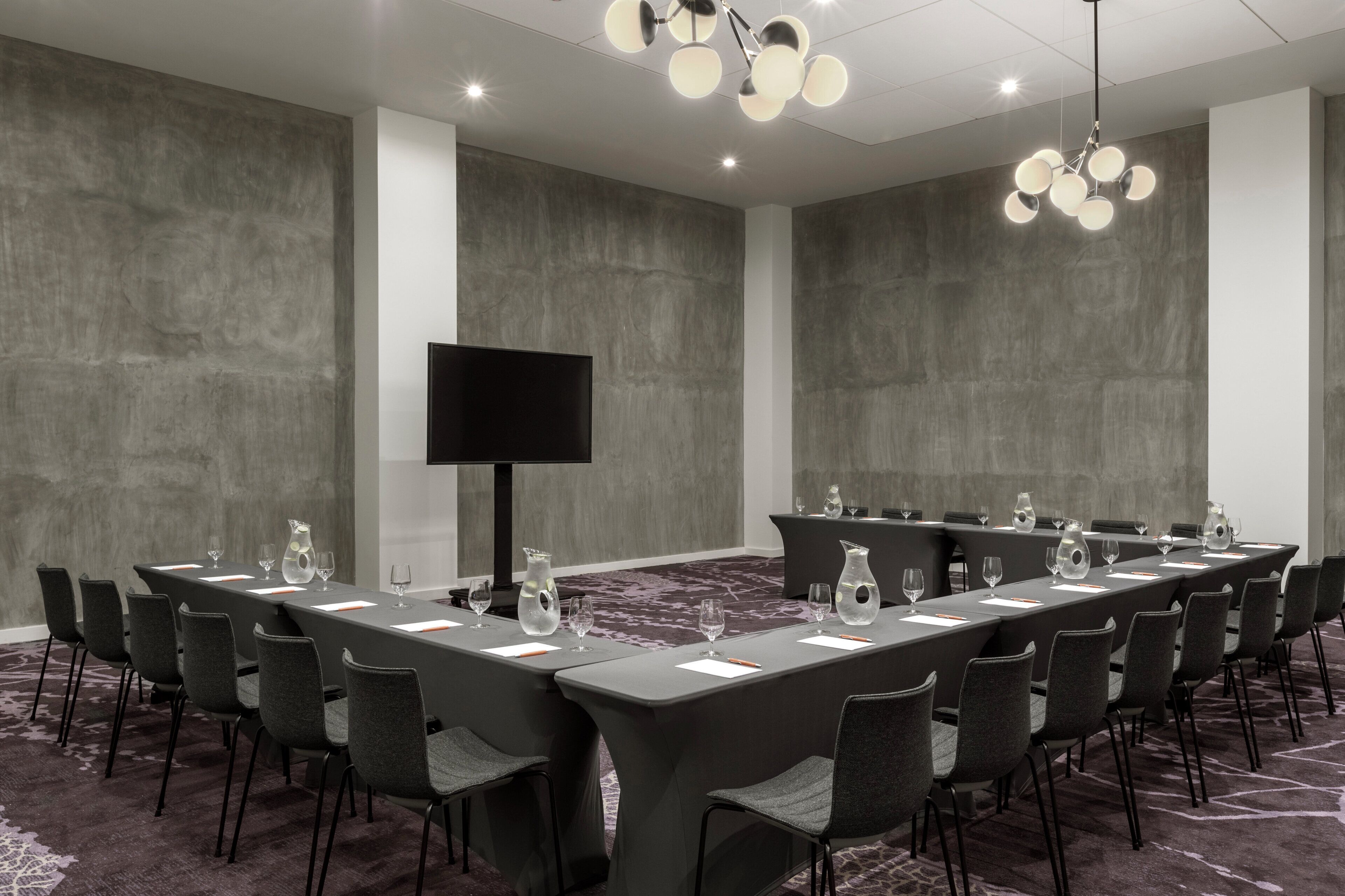 A conference room with a long table, chairs, a flat-screen TV, and a chandelier.