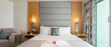 A hotel room with a large bed, two bedside tables, a nightstand, a sofa, and a large window with curtains.