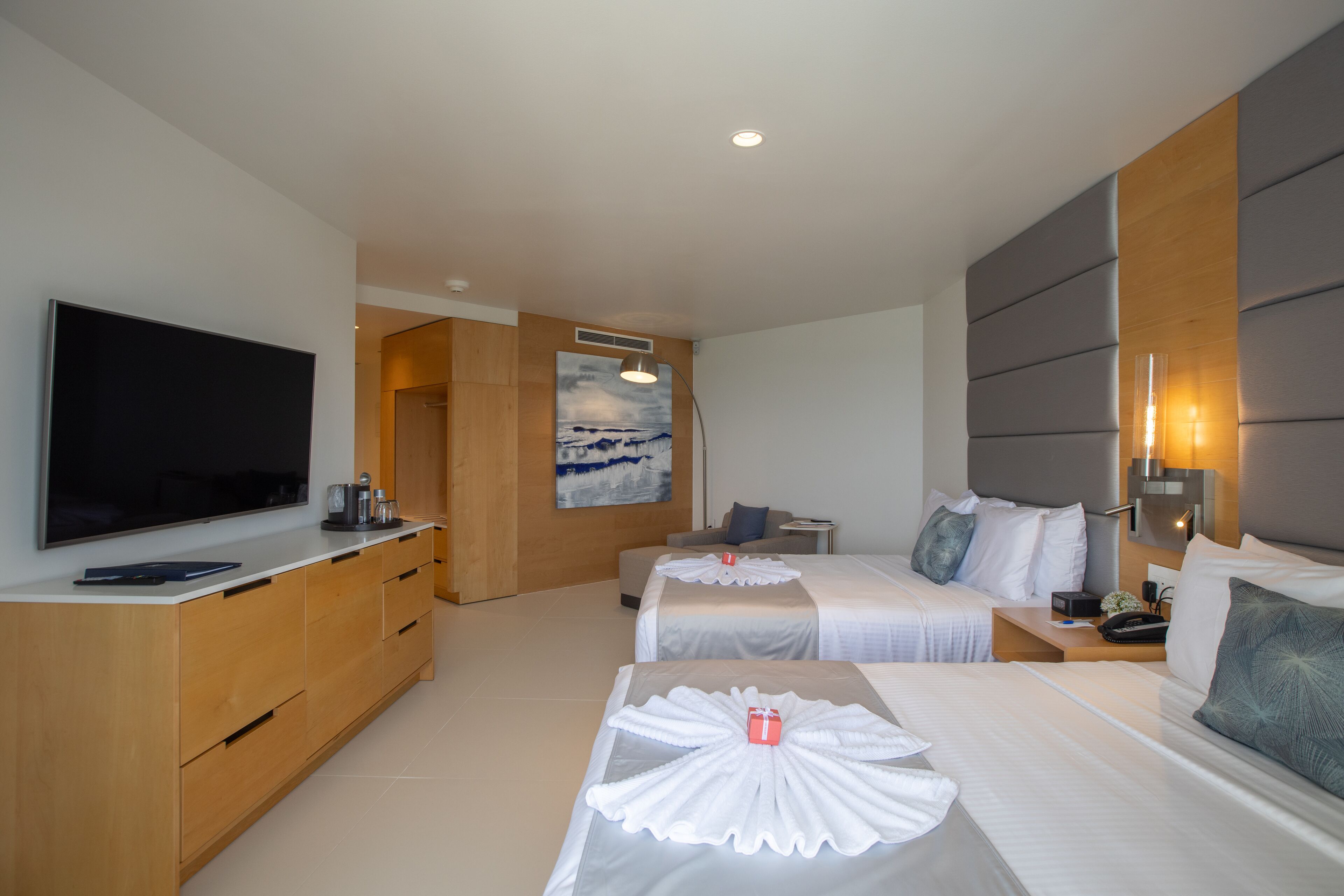 Una habitación de hotel con dos camas, un televisor, un aparador de madera y un cuadro en la pared.