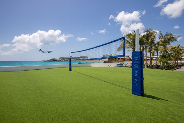 A beach volleyball court with a net, palm trees, and a hotel named "The Morgan" in the background. - The Morgan Resort Spa Village (Simpson Bay)