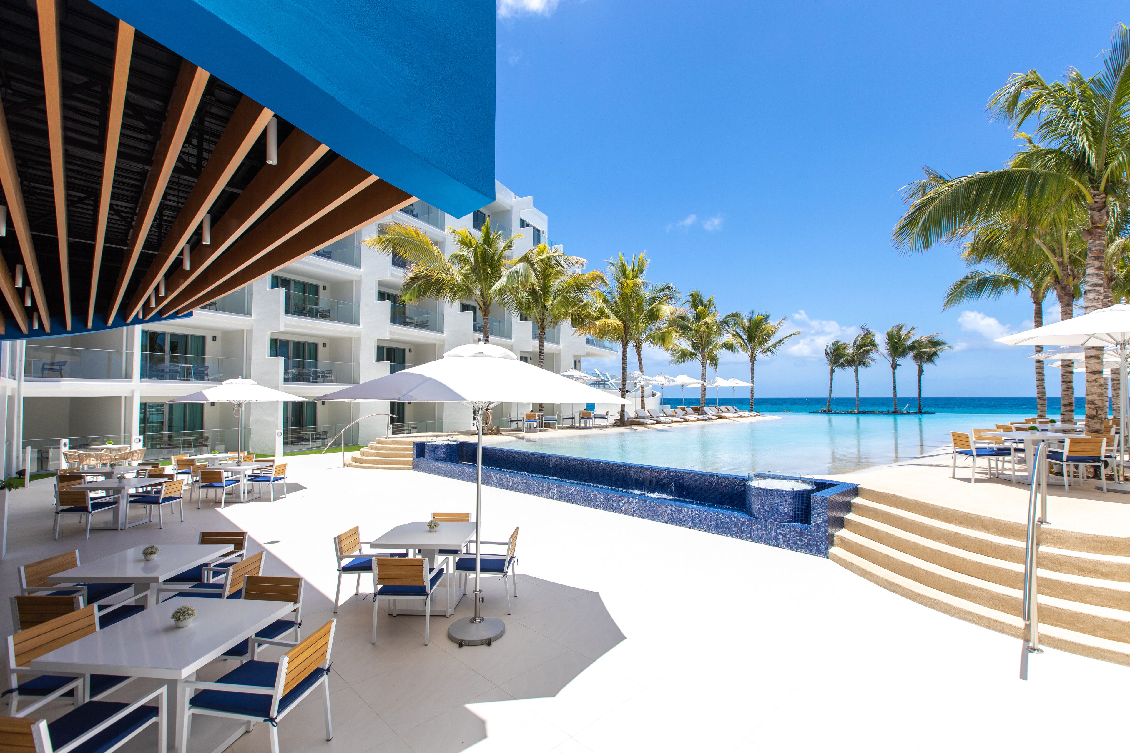Zona de piscina en un resort con mobiliario exterior y vista al océano.