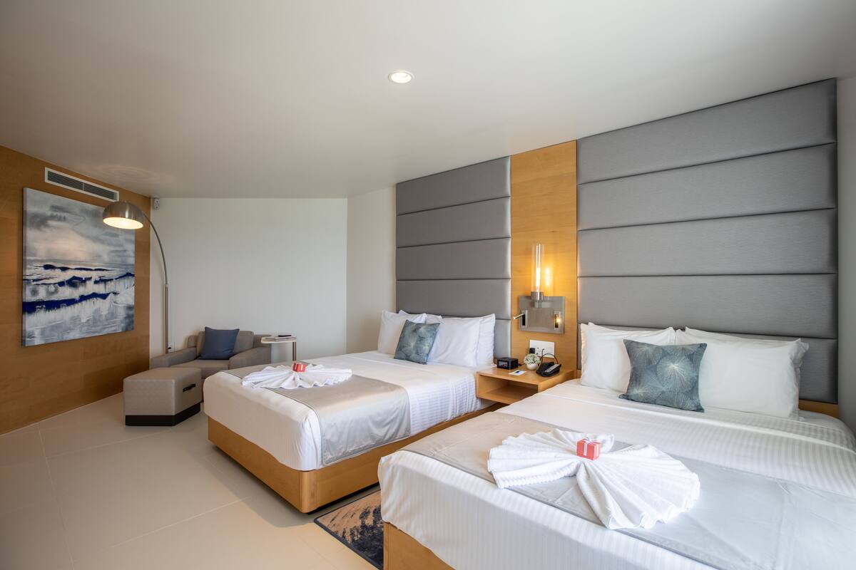 A hotel room with two beds, a sofa, a desk, and a painting on the wall.