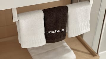 Un baño con un toallero blanco que sostiene dos toallas, una blanca y otra marrón con la palabra 'makeup' escrita.
