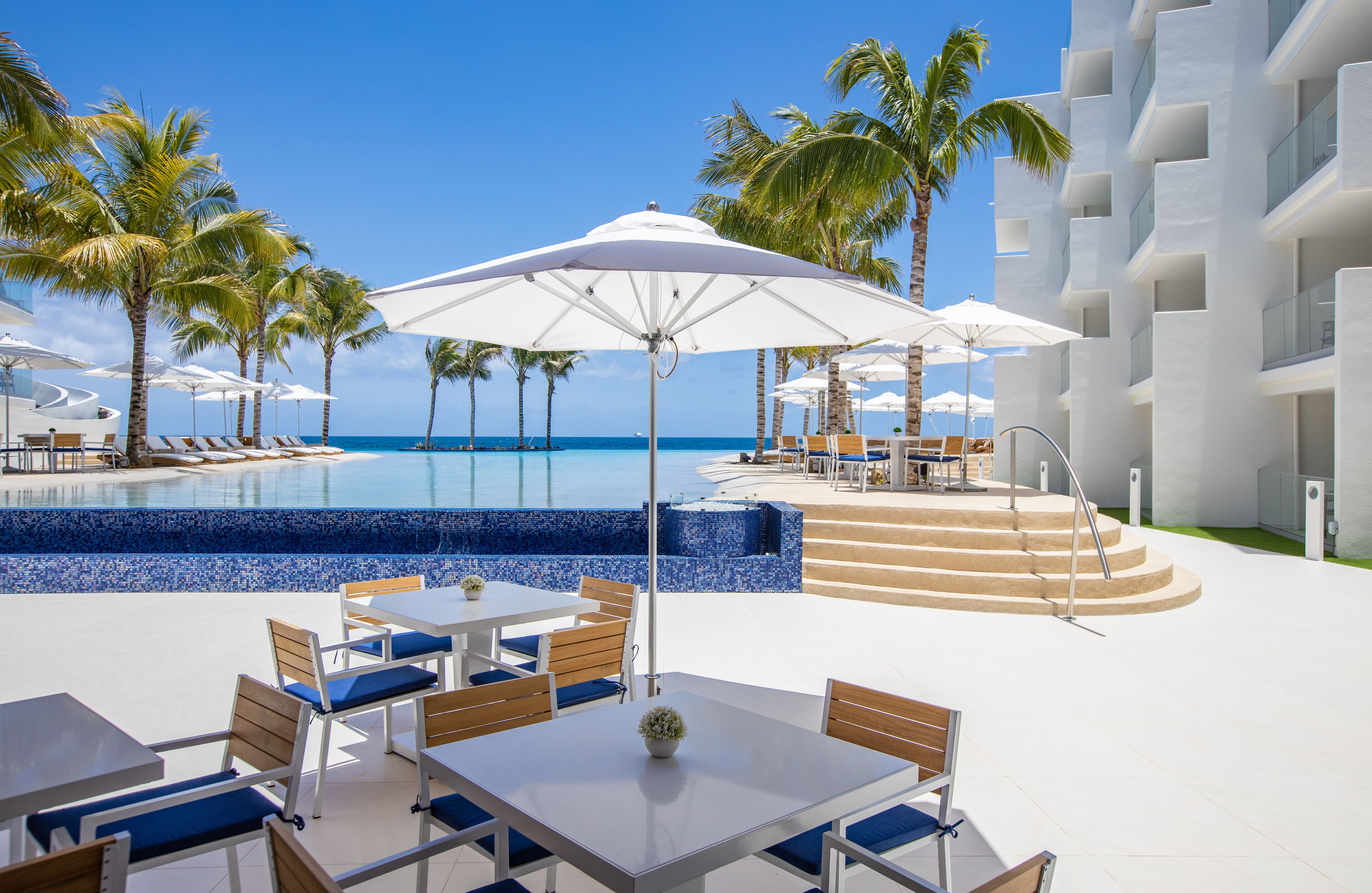 A resort pool area with sun loungers, umbrellas, and a clear view of the ocean.