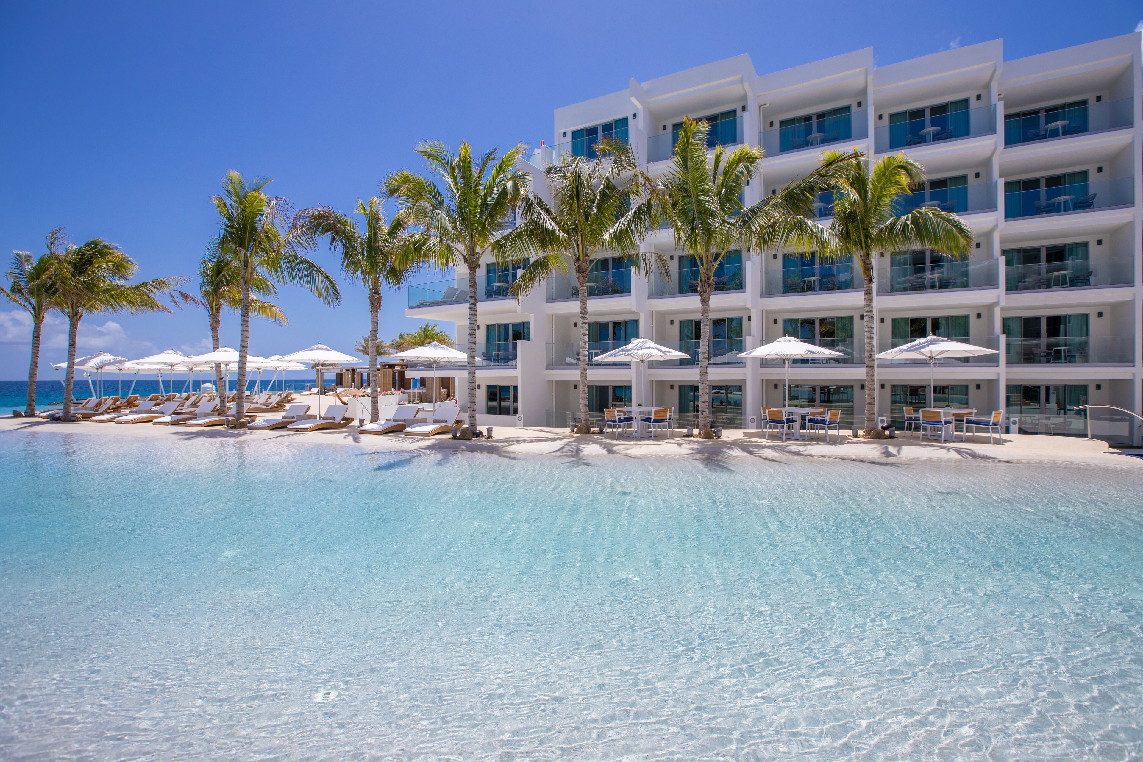 A hotel with a pool, palm trees, and beach chairs.