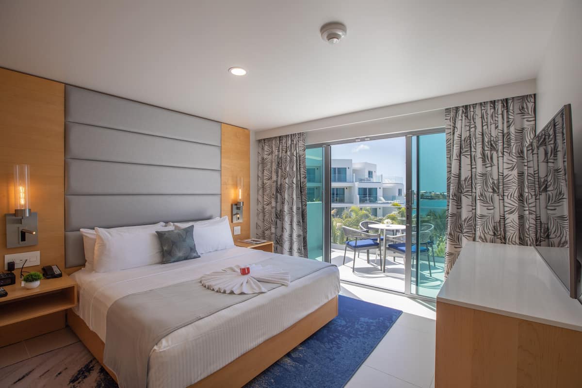 A modern hotel room with a large bed, a desk, and a balcony with a view of the city.