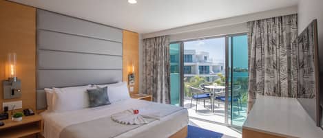 A modern hotel room with a large bed, a desk, and a balcony with a view of the city.