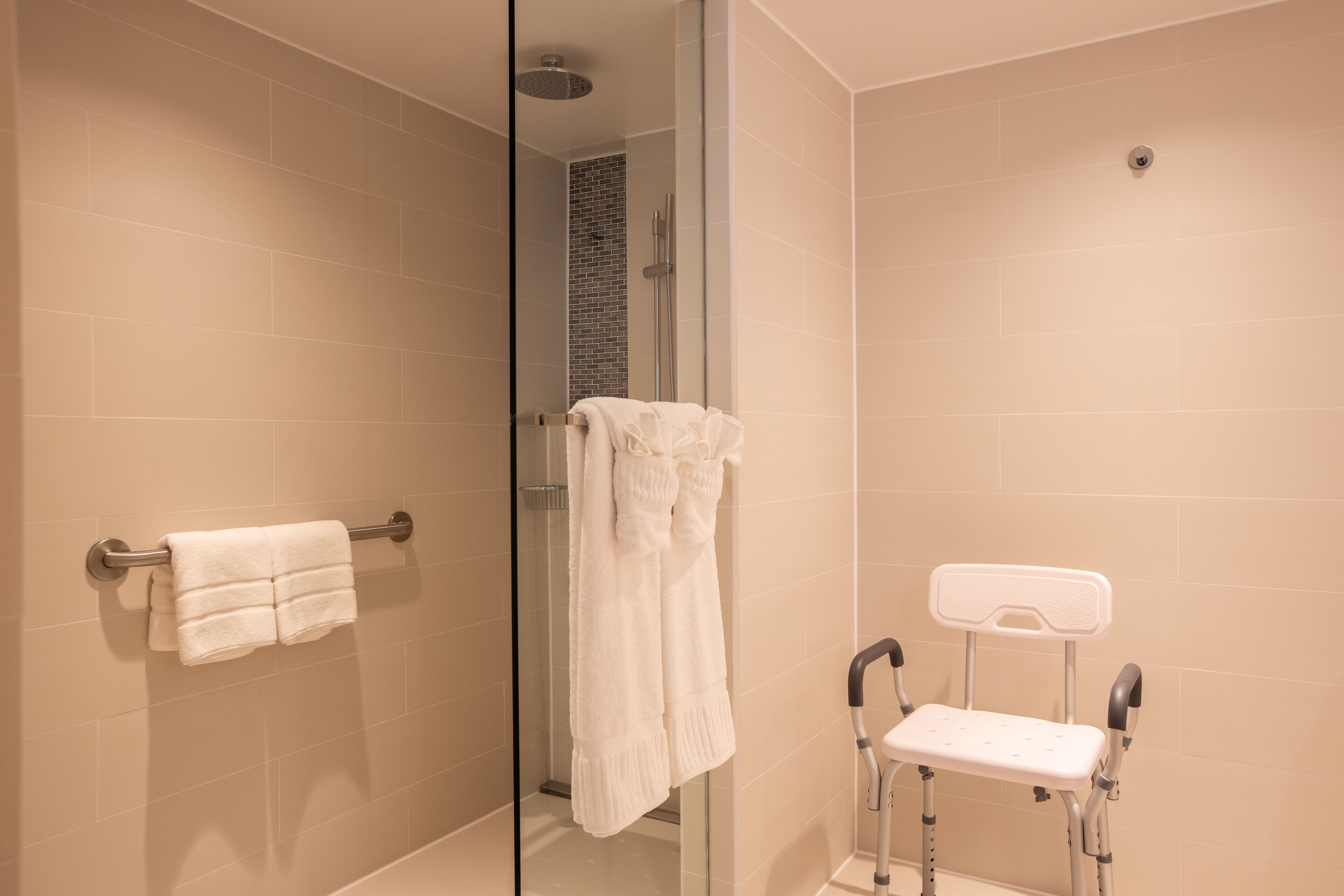 A bathroom with beige tiles, a glass shower enclosure, a white towel rack, and a mobility aid.