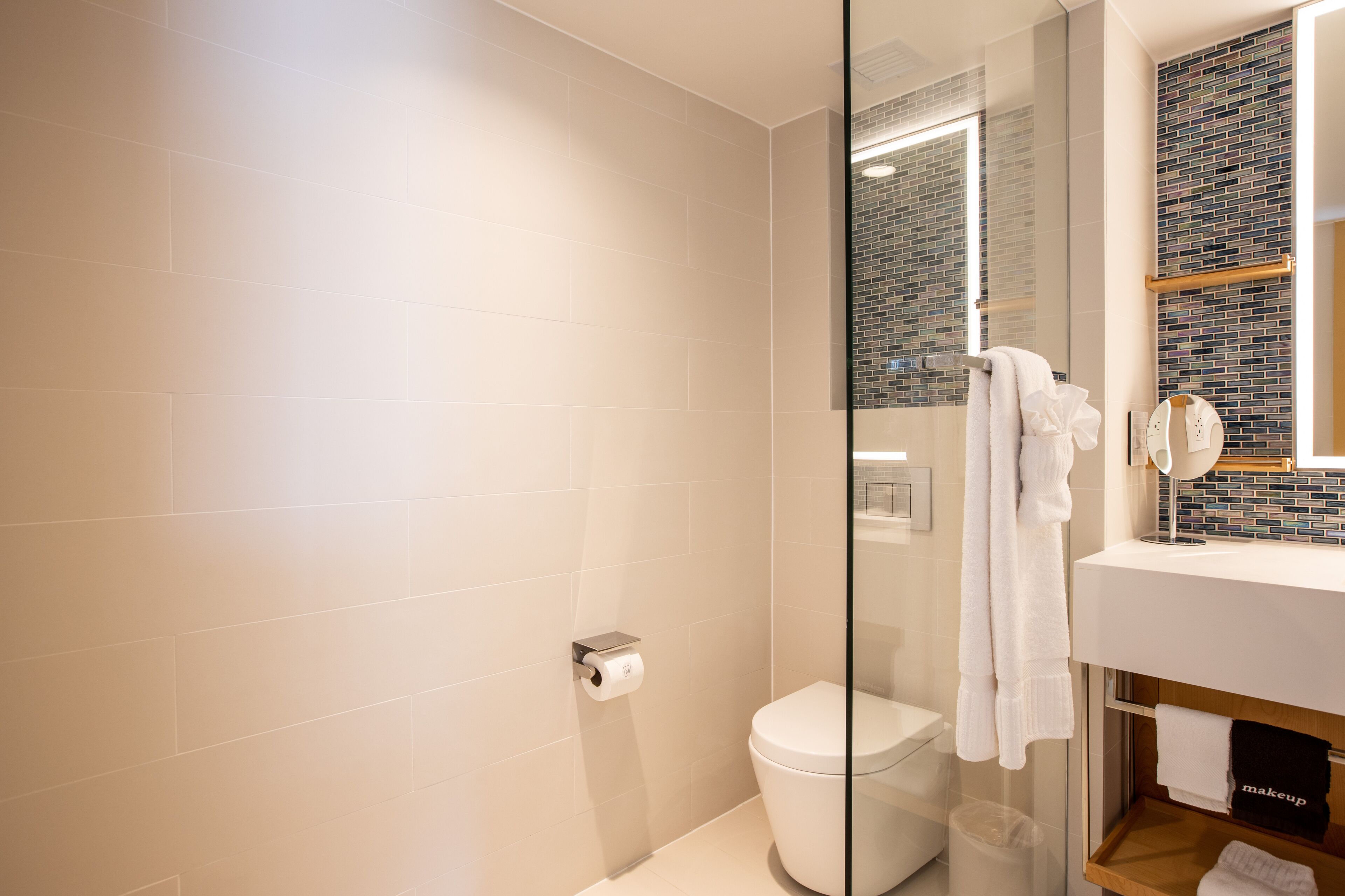 A modern bathroom with a glass shower enclosure, a toilet, and a vanity with a mirror and towel rack.