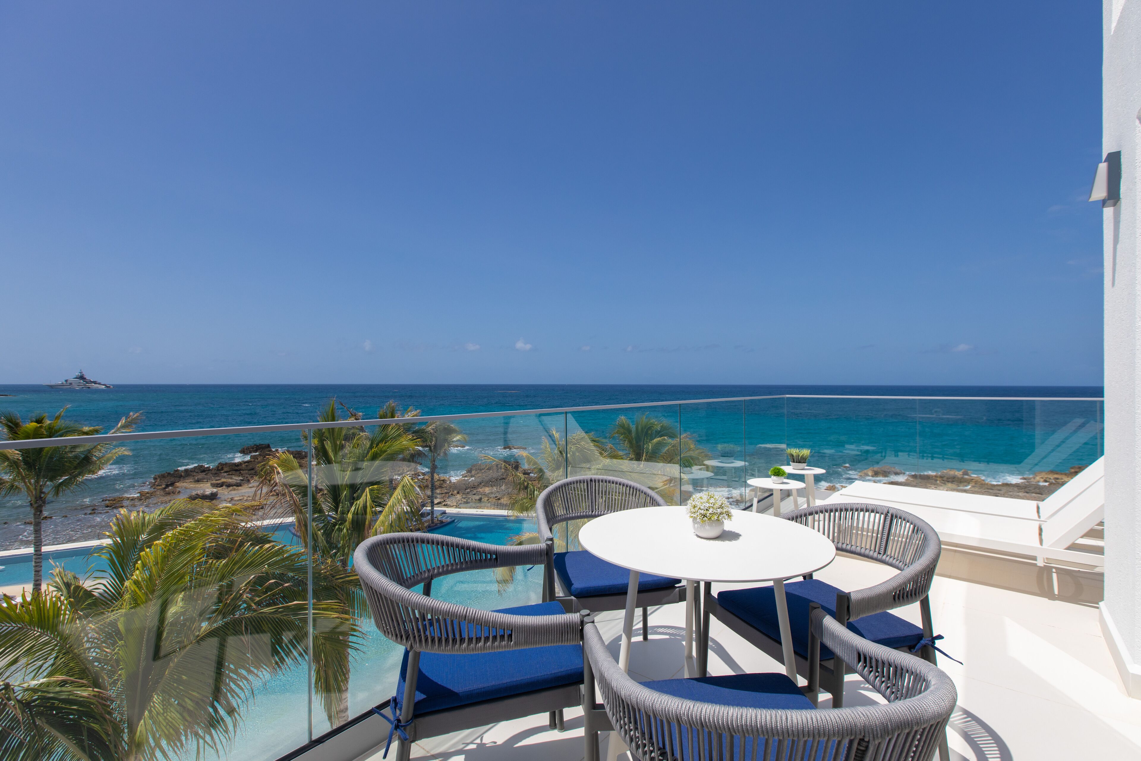 A balcony with wicker furniture, a small table, and a view of the ocean.
