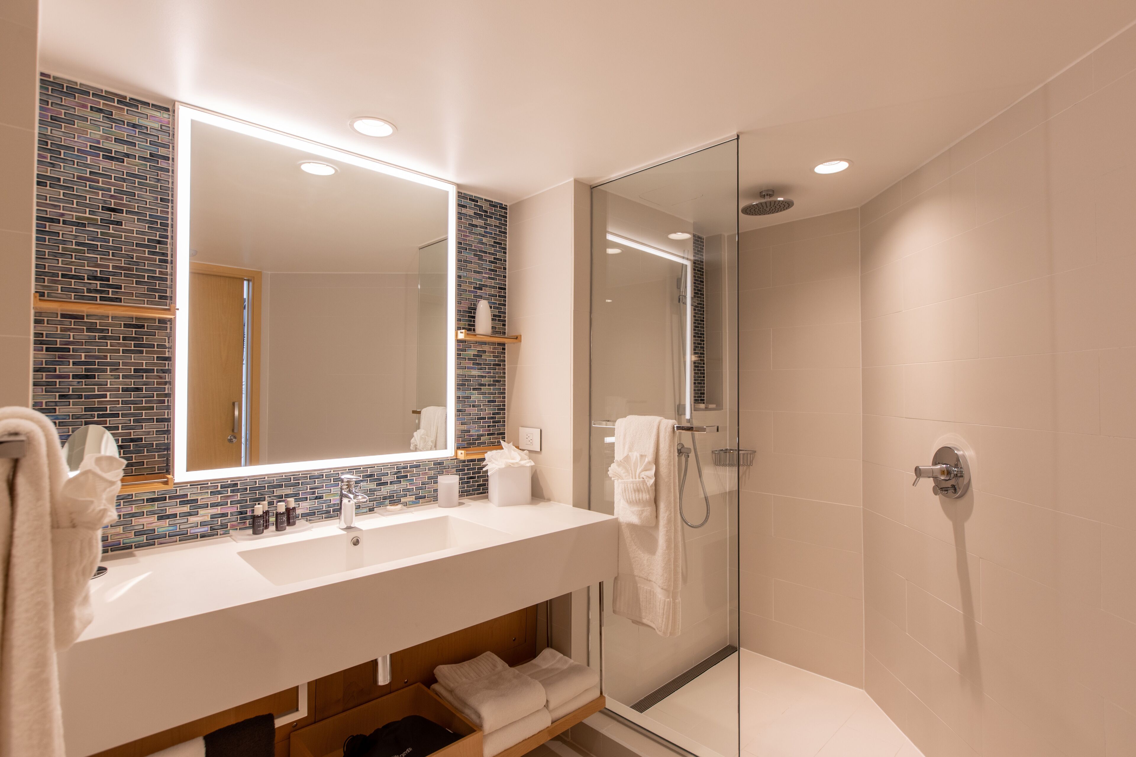 Un baño moderno con cabina de ducha de vidrio, un lavabo blanco con espejo y un salpicadero de azulejos.