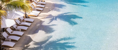 An aerial view of a resort with a clear blue pool, sun loungers, and palm trees.