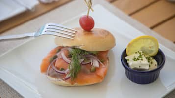 Un sándwich con una cereza encima, una rodaja de limón y un recipiente pequeño de salsa sobre un plato blanco.