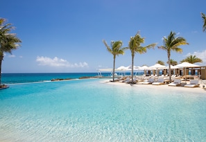 A clear blue pool with lounge chairs and palm trees, overlooking the ocean. - The Morgan Resort Spa Village (Simpson Bay)