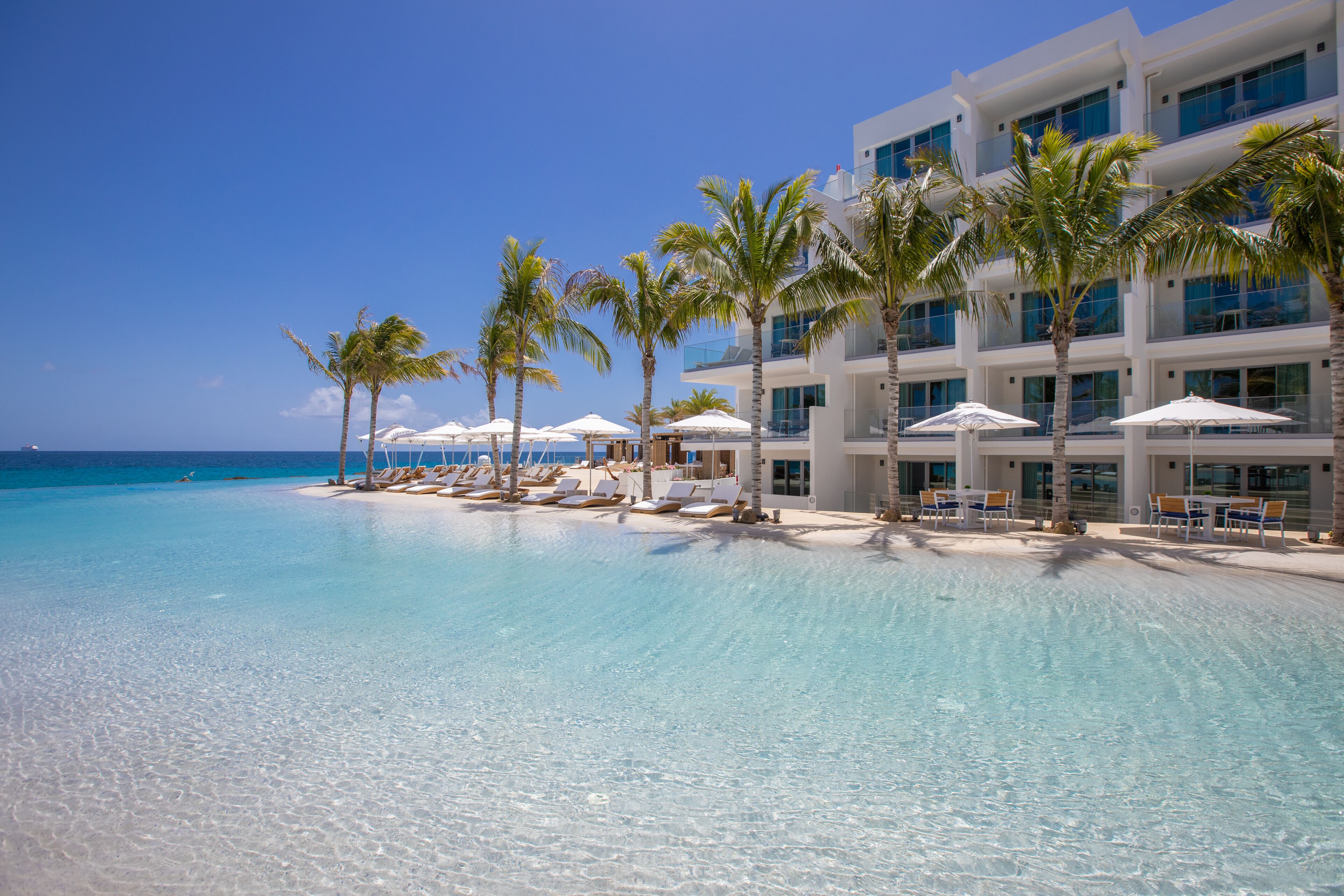 Un resort con piscina azul cristalina, palmeras y sillas de playa.