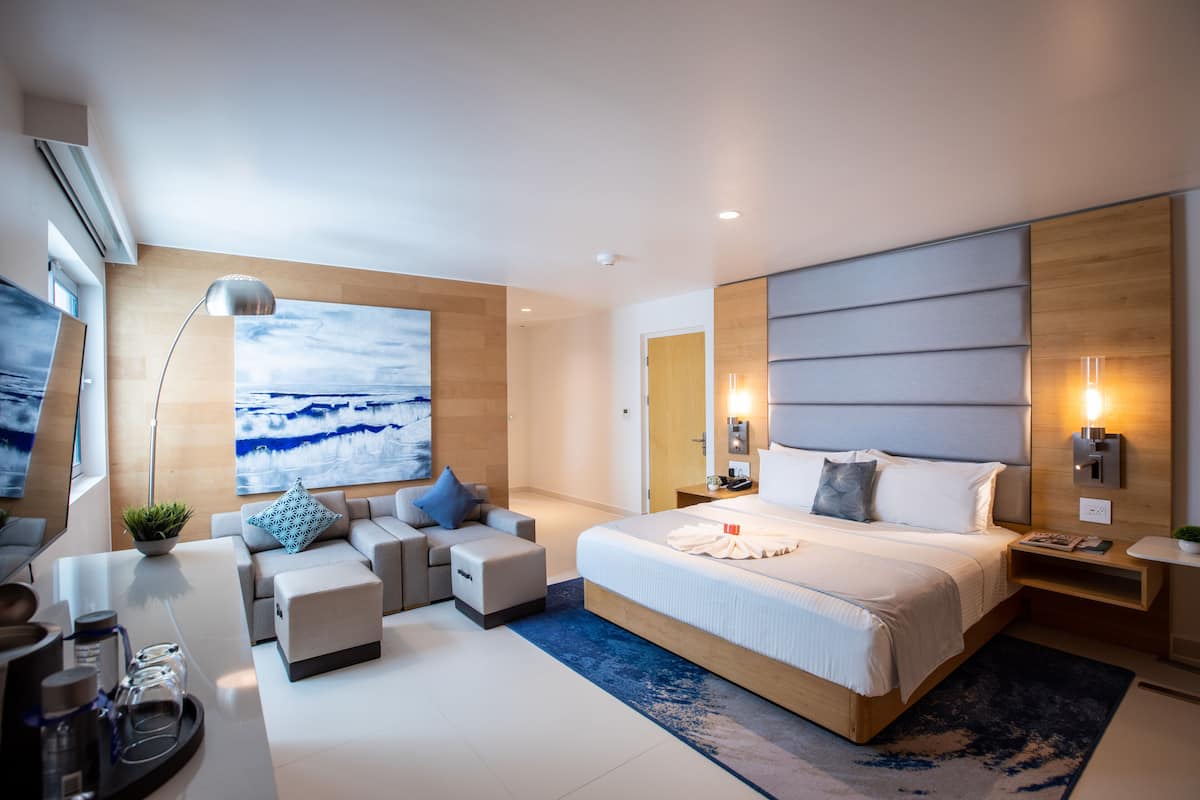 A modern hotel room with a large bed, a sofa, a coffee table, and a TV.