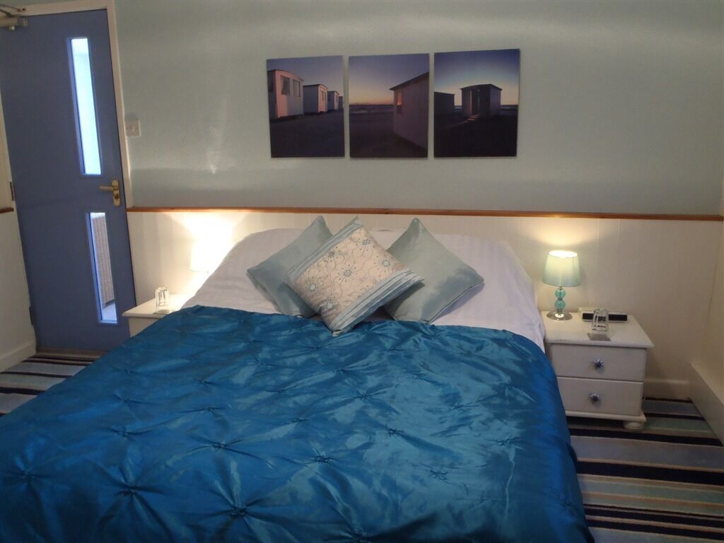 A bedroom with a bed, pillows, a nightstand, a lamp, and three wall-mounted pictures.