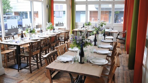 A dining area with multiple tables set for a meal, large windows, and a view of the street outside. - The Grange Pub (London)