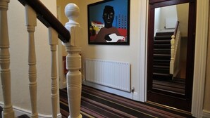 A staircase with striped carpet leading to a room with a white radiator and a framed artwork on the wall. - The Grange Pub (London)