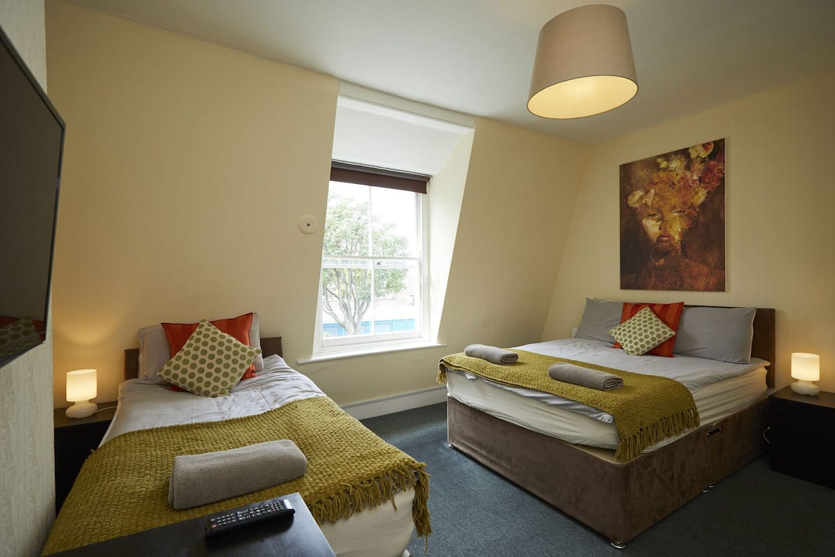 A hotel room with two beds, a large window, and a painting on the wall.