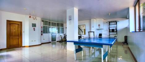 Amplia habitación con mesa de ping pong, una puerta de madera y una bicicleta al fondo.