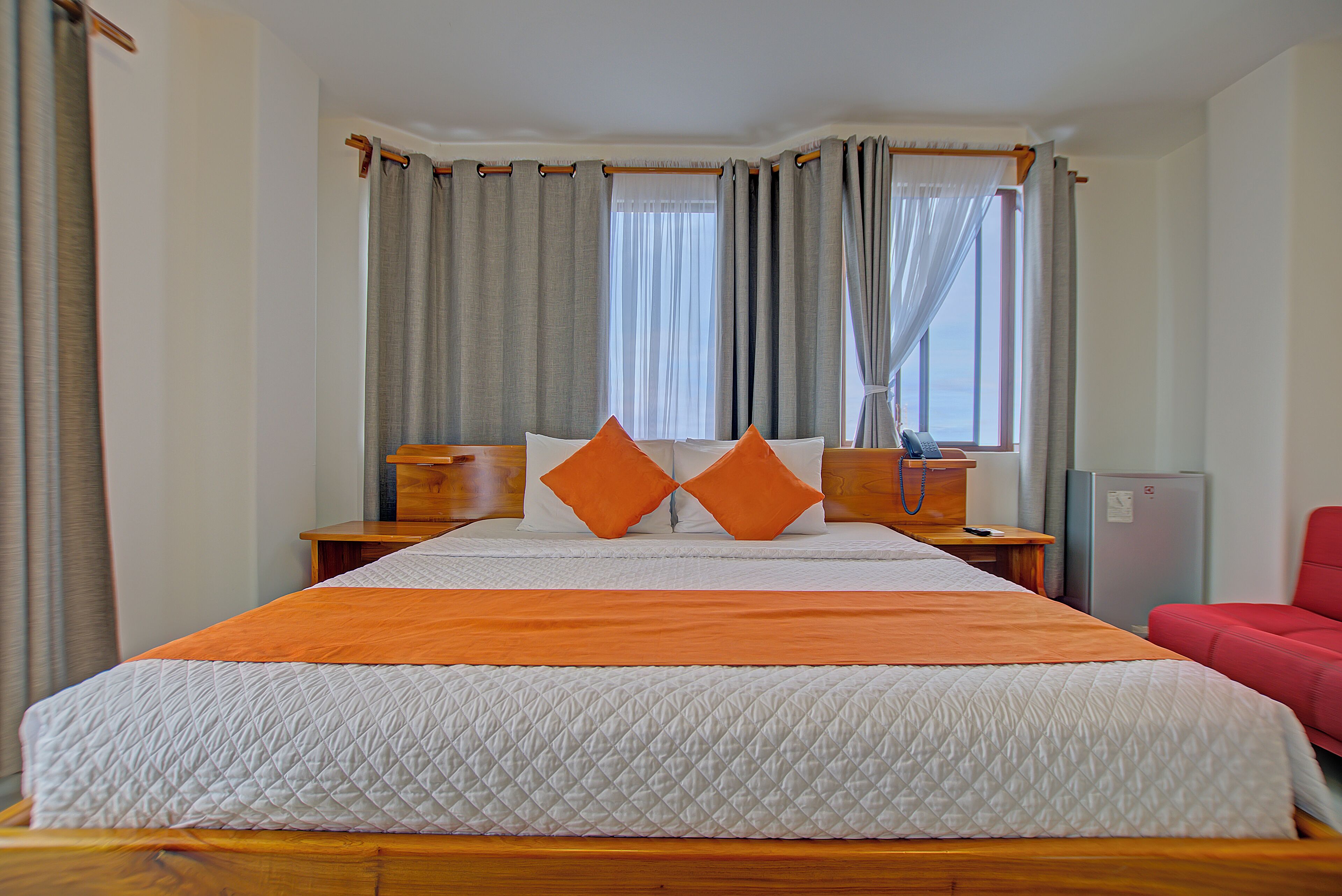 A hotel room with a large bed, two nightstands, a red chair, and a window with curtains.