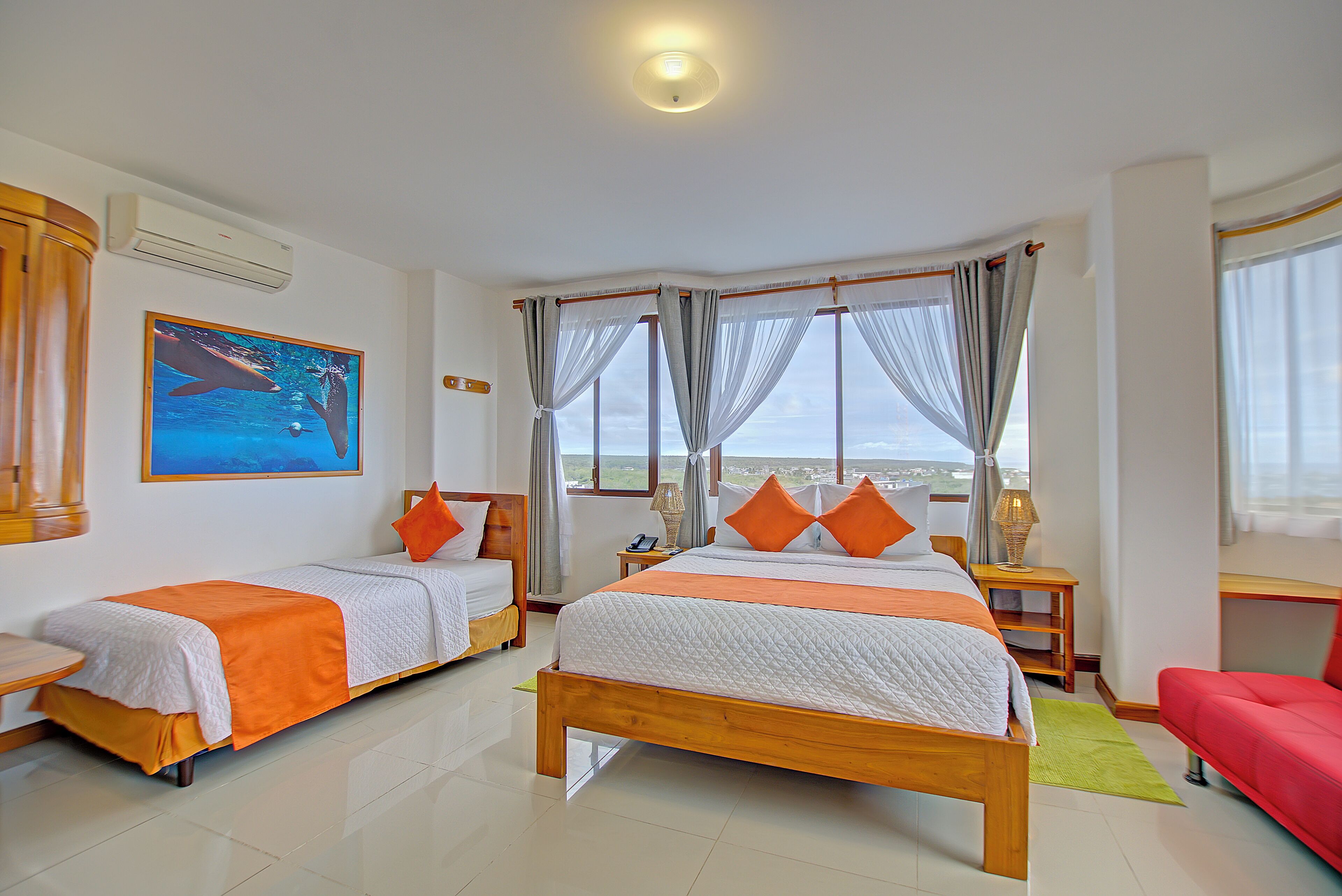 Habitación de hotel con dos camas, un ventanal con cortinas, un cuadro en la pared y un sofá rojo.