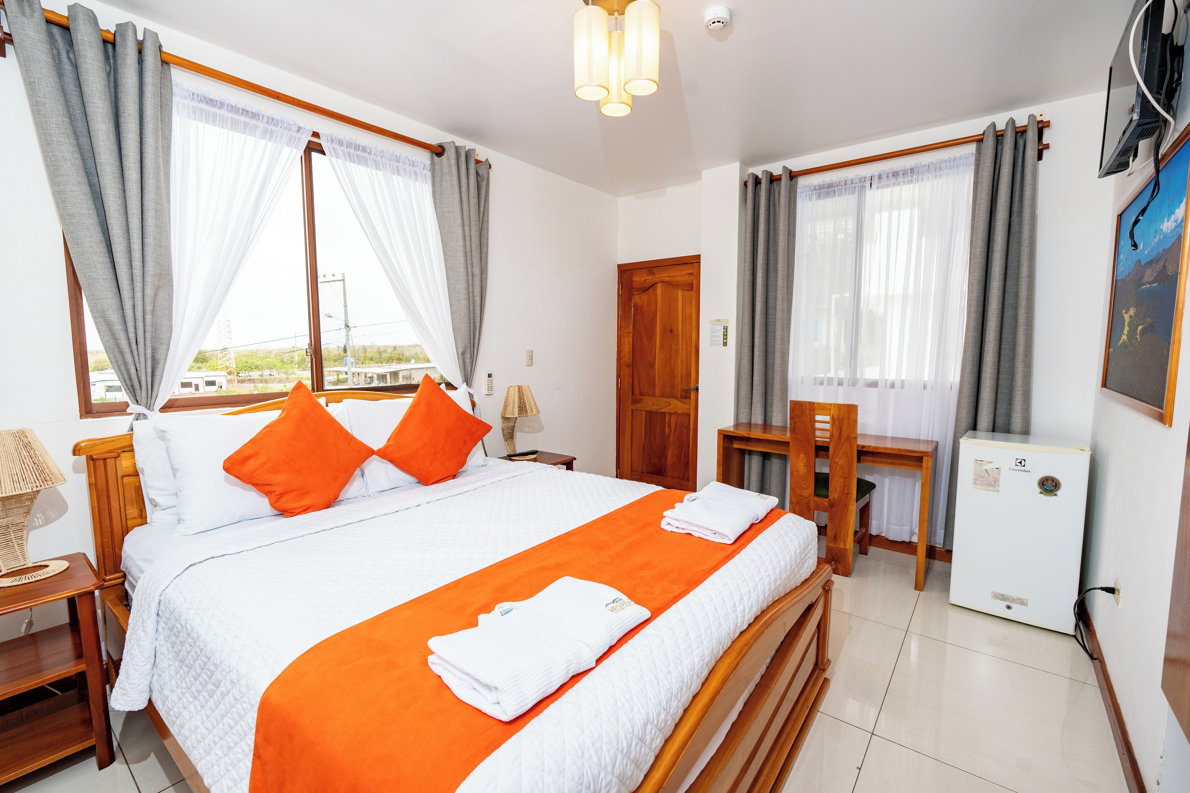 Una habitación de hotel con cama, escritorio, silla, refrigerador y cortinas.