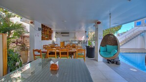 Un espace piscine intérieur moderne, avec une table en verre, des chaises en bois et un fauteuil suspendu près de la piscine.