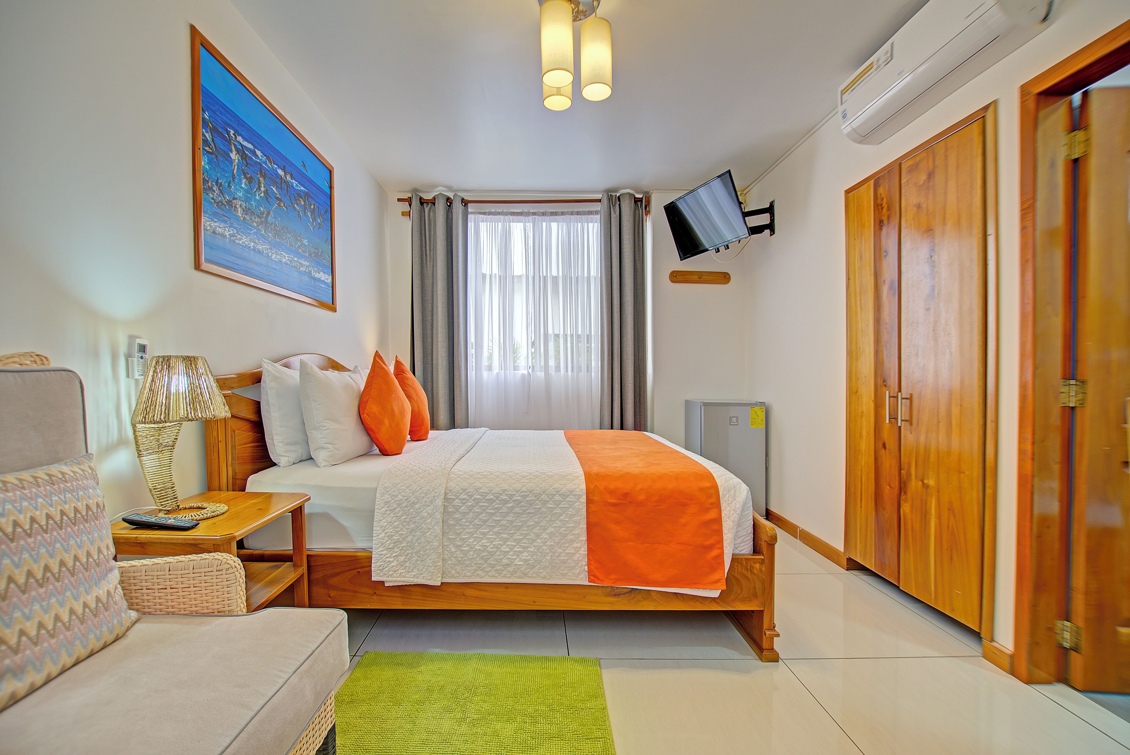 A hotel room with a bed, a television mounted on the wall, a wardrobe, and a painting on the wall.